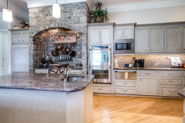 kitchen with appliances with stainless steel finishes, sink, dark stone countertops, hanging light fixtures, and light hardwood / wood-style floors