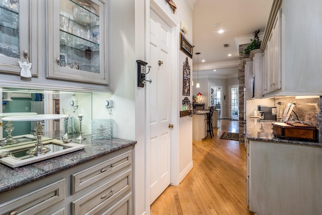 bar featuring tasteful backsplash, dark stone countertops, hanging light fixtures, ornamental molding, and light wood-type flooring