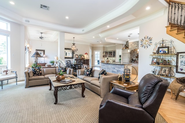 living room with crown molding, a tray ceiling, ceiling fan with notable chandelier, and light hardwood / wood-style flooring