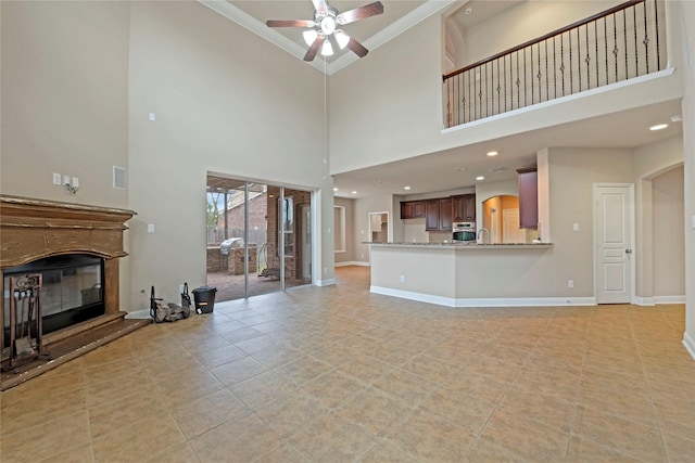 unfurnished living room with sink, ceiling fan, a high ceiling, ornamental molding, and light tile patterned flooring