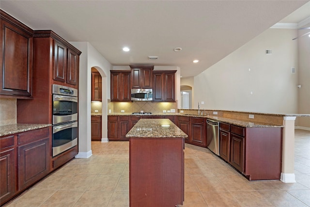 kitchen featuring a center island, light tile patterned floors, kitchen peninsula, stainless steel appliances, and light stone countertops