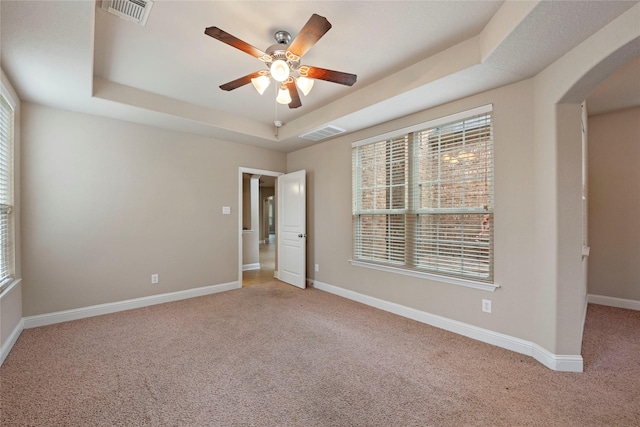 empty room with ceiling fan, light colored carpet, and a raised ceiling