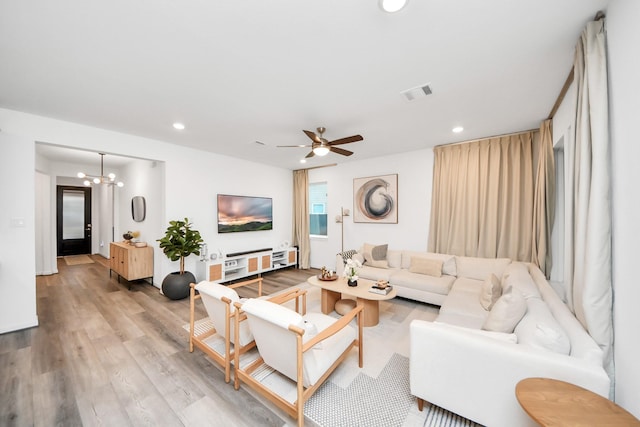 living room featuring ceiling fan with notable chandelier and light wood-type flooring