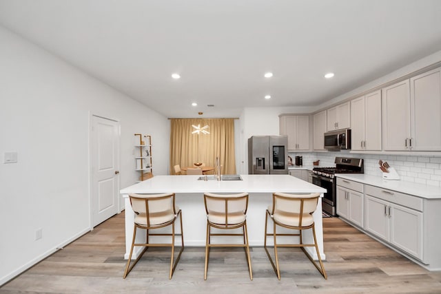 kitchen featuring tasteful backsplash, a kitchen bar, a center island with sink, and appliances with stainless steel finishes