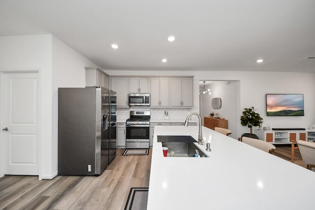 kitchen with stainless steel appliances, sink, backsplash, and light hardwood / wood-style flooring