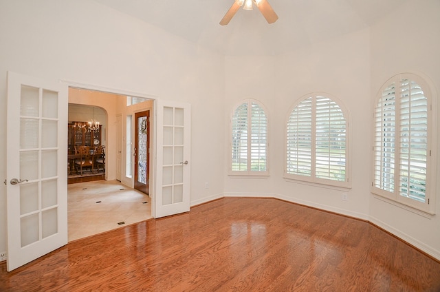 spare room featuring ceiling fan with notable chandelier, wood-type flooring, french doors, and a towering ceiling