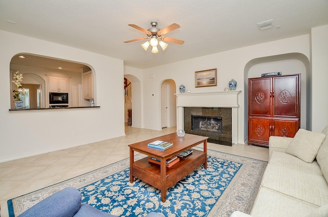 living room featuring ceiling fan, a high end fireplace, a textured ceiling, and light tile patterned flooring