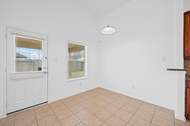 unfurnished dining area with light tile patterned floors and high vaulted ceiling