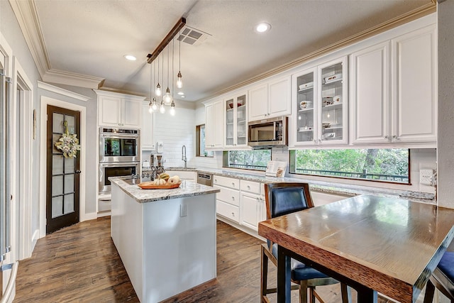 kitchen with a kitchen island, appliances with stainless steel finishes, pendant lighting, white cabinetry, and sink