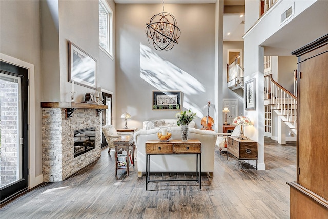 living room featuring hardwood / wood-style flooring, a towering ceiling, an inviting chandelier, and a fireplace