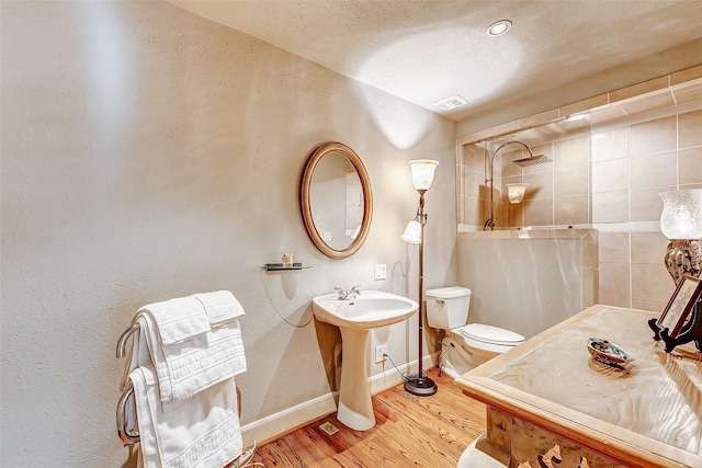 bathroom with wood-type flooring, tiled shower, a textured ceiling, and toilet