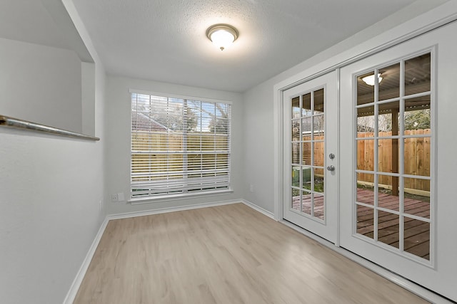 unfurnished dining area featuring a textured ceiling, light hardwood / wood-style floors, and french doors