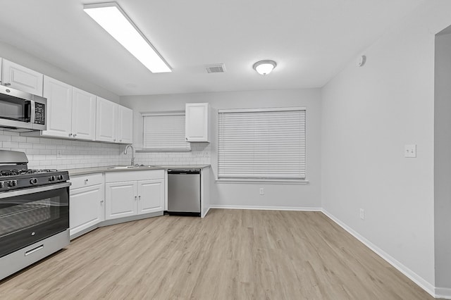 kitchen with appliances with stainless steel finishes, tasteful backsplash, sink, white cabinets, and light hardwood / wood-style floors