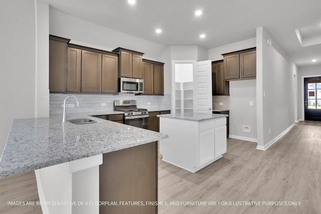 kitchen featuring a peninsula, light stone countertops, stainless steel appliances, light wood-type flooring, and a sink