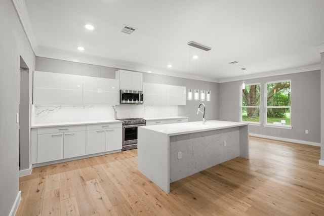 kitchen with a center island with sink, white cabinets, pendant lighting, stainless steel appliances, and backsplash