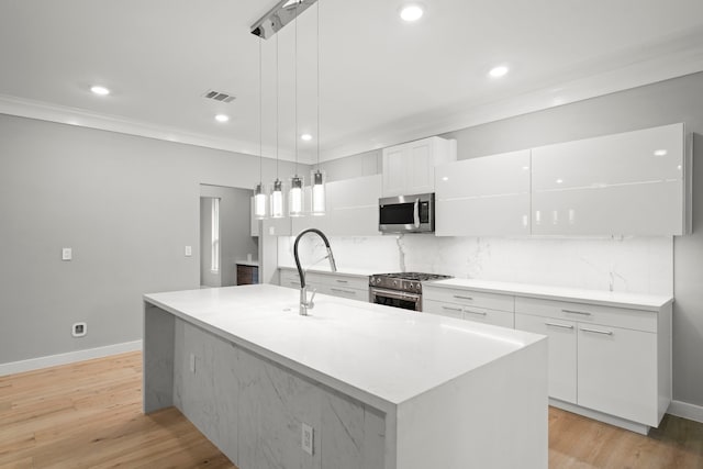 kitchen featuring white cabinetry, appliances with stainless steel finishes, hanging light fixtures, and a center island with sink