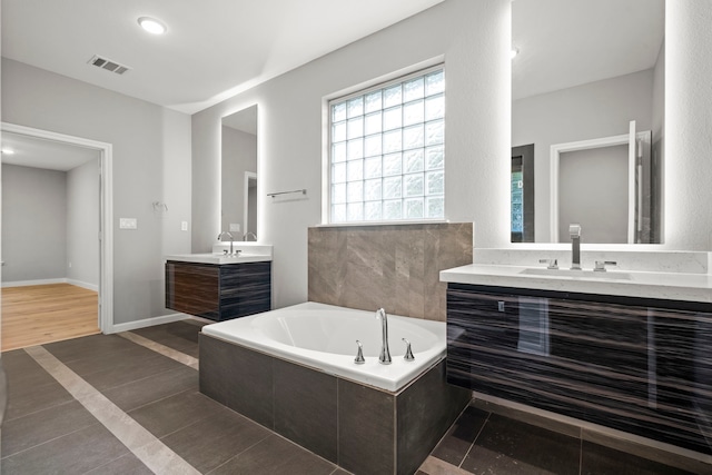 bathroom featuring a relaxing tiled tub, tile patterned floors, and vanity