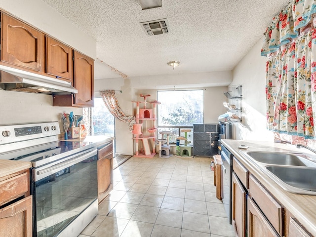 kitchen with appliances with stainless steel finishes, sink, light tile patterned floors, and a textured ceiling