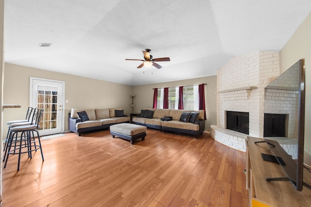 living room featuring vaulted ceiling, a brick fireplace, hardwood / wood-style floors, and ceiling fan