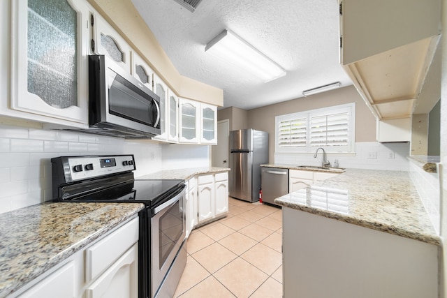 kitchen featuring light tile patterned floors, sink, appliances with stainless steel finishes, light stone counters, and white cabinets