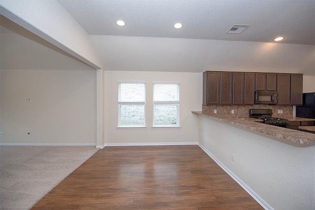 kitchen with dark hardwood / wood-style floors, black appliances, backsplash, light stone counters, and kitchen peninsula