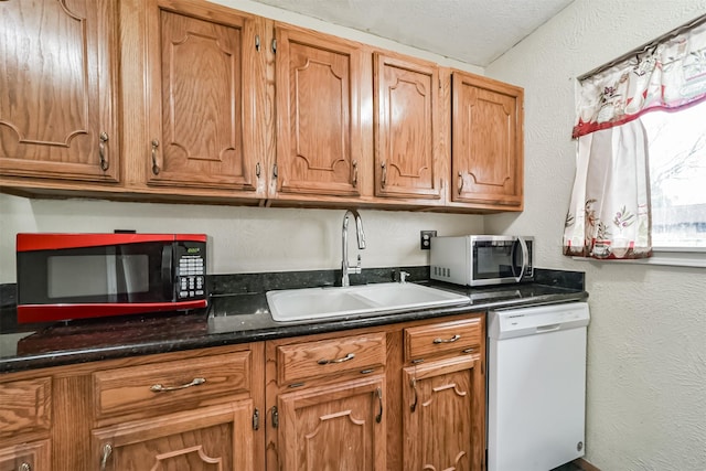 kitchen featuring white dishwasher, sink, and dark stone counters