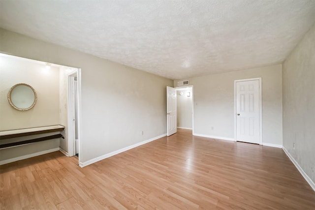 empty room with a textured ceiling and light hardwood / wood-style flooring