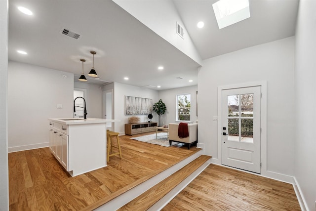 kitchen with sink, light hardwood / wood-style flooring, a breakfast bar, hanging light fixtures, and white cabinets