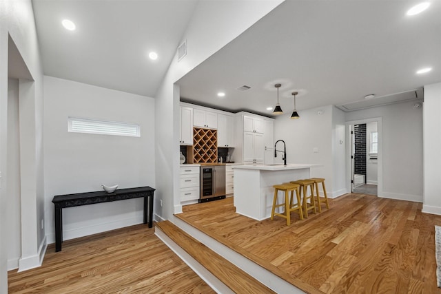 kitchen featuring a breakfast bar area, white cabinetry, hanging light fixtures, beverage cooler, and light wood-type flooring