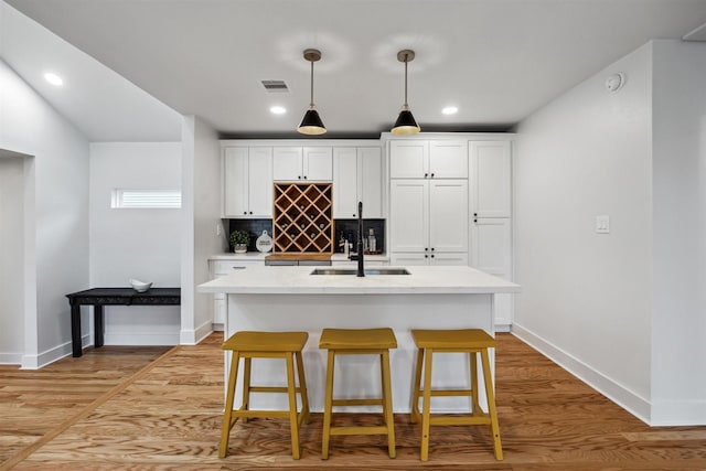 kitchen featuring tasteful backsplash, white cabinetry, a kitchen island with sink, and light hardwood / wood-style flooring