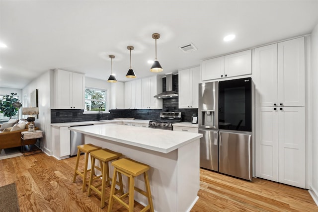 kitchen featuring sink, white cabinets, hanging light fixtures, stainless steel appliances, and wall chimney exhaust hood