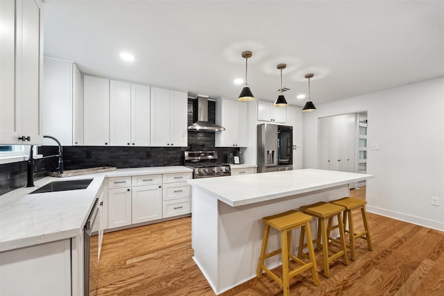 kitchen with appliances with stainless steel finishes, sink, white cabinets, a center island, and wall chimney exhaust hood