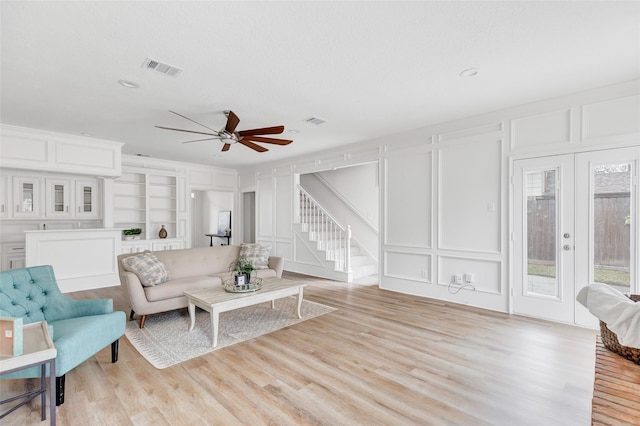 living room featuring built in features, light hardwood / wood-style floors, ceiling fan, and french doors