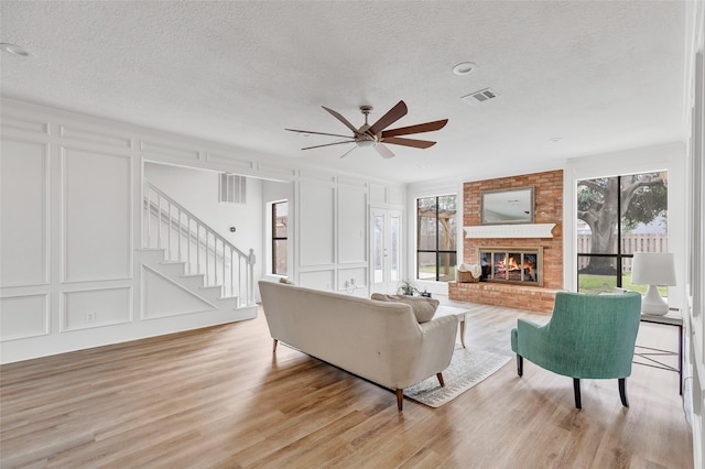 living room featuring a brick fireplace, ceiling fan, a textured ceiling, and light wood-type flooring