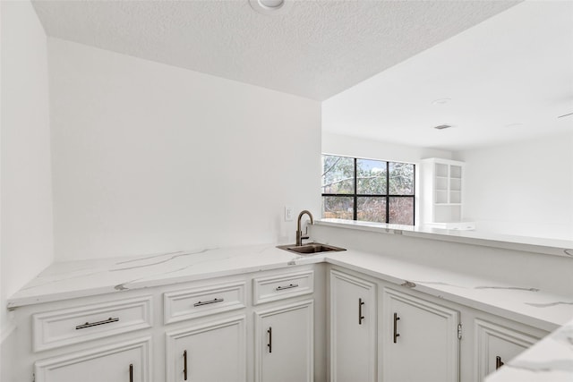 kitchen with sink, a textured ceiling, light stone countertops, and white cabinets