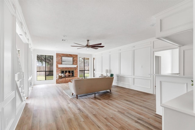 living room featuring ceiling fan, light hardwood / wood-style floors, a brick fireplace, and a textured ceiling