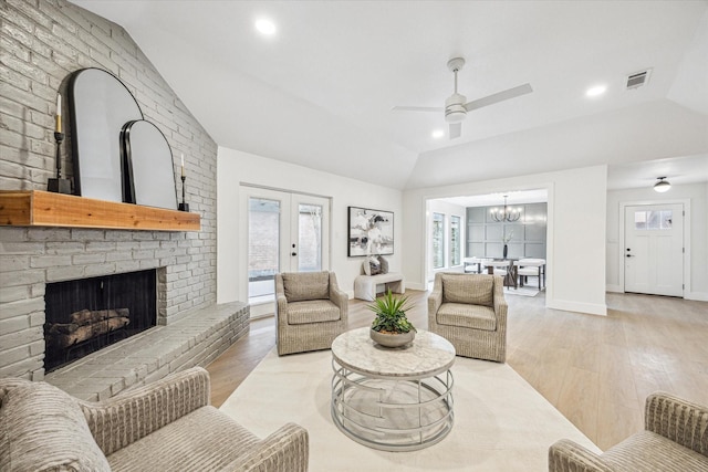 living room with french doors, vaulted ceiling, light wood-type flooring, a fireplace, and ceiling fan with notable chandelier