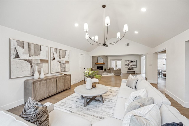 living room featuring lofted ceiling, hardwood / wood-style floors, a chandelier, and a brick fireplace