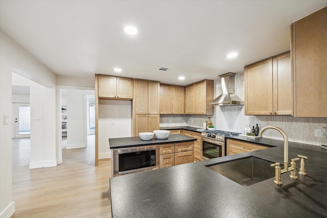 kitchen with gas stove, sink, wall chimney range hood, and light brown cabinetry