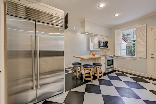 kitchen featuring stainless steel appliances, white cabinetry, crown molding, and butcher block countertops