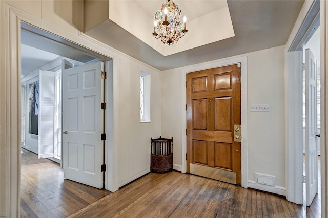 foyer with an inviting chandelier, hardwood / wood-style floors, and a tray ceiling