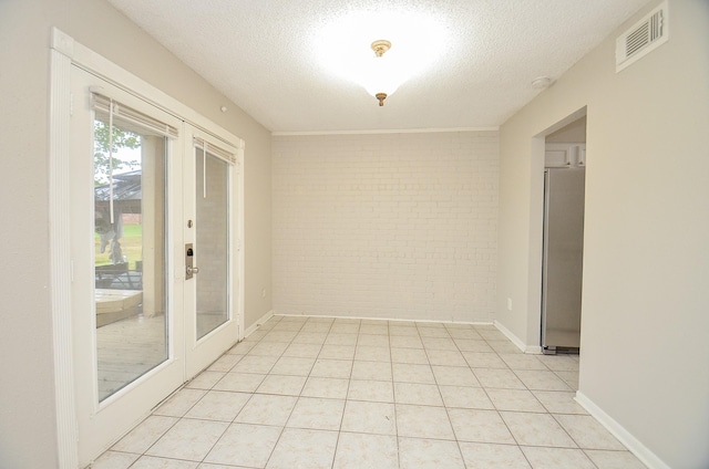 empty room featuring light tile patterned floors, french doors, a textured ceiling, and brick wall