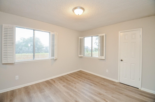 unfurnished room with plenty of natural light, light hardwood / wood-style floors, and a textured ceiling