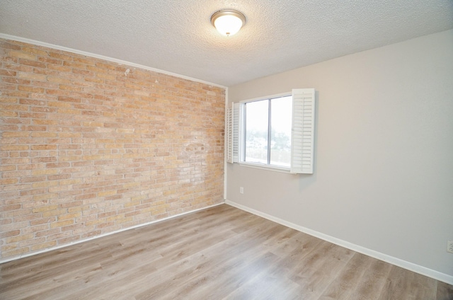 unfurnished room with light hardwood / wood-style floors, a textured ceiling, and brick wall