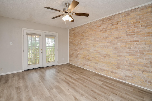 unfurnished room featuring brick wall, light wood-type flooring, ceiling fan, a textured ceiling, and french doors