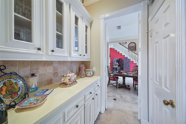 bar with tasteful backsplash, ornamental molding, and white cabinets