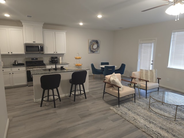 kitchen featuring white cabinetry, tasteful backsplash, dark stone countertops, an island with sink, and stainless steel appliances