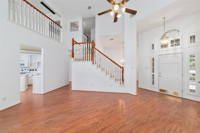 entrance foyer with a towering ceiling, wood-type flooring, and ceiling fan with notable chandelier