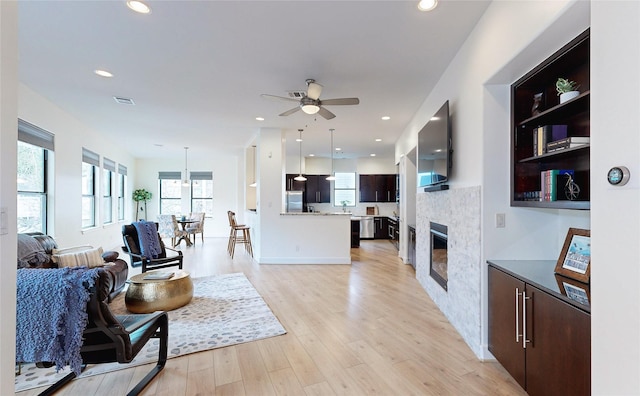 living room featuring ceiling fan, a tiled fireplace, and light hardwood / wood-style flooring