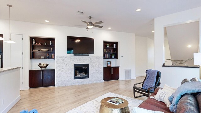 living room featuring ceiling fan, light hardwood / wood-style floors, and built in shelves